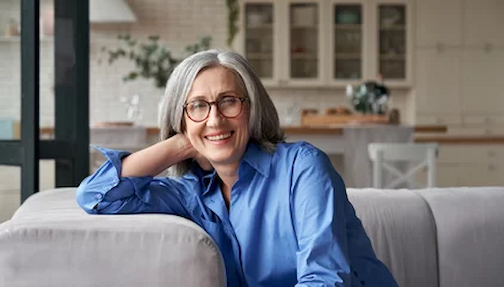 Happy relaxed mature old adult woman wearing glasses resting sitting on couch at home