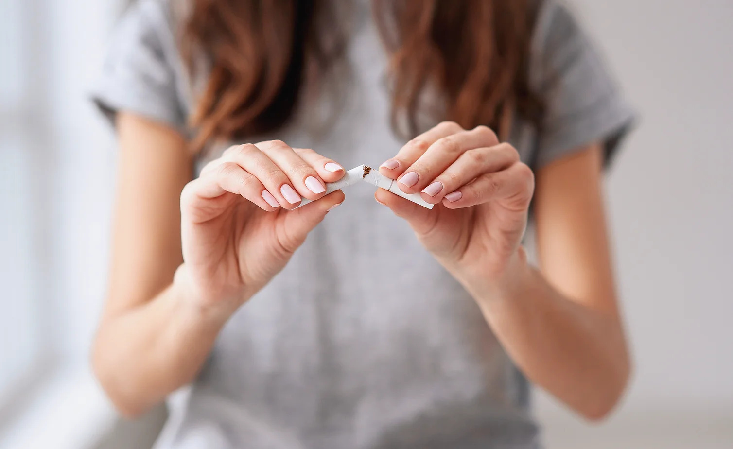 Stop smoking cigarettes concept. Portrait of beautiful smiling girl holding broken cigarette in hands. 