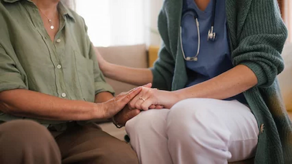 Close-up of nurse holding hand to senior client.